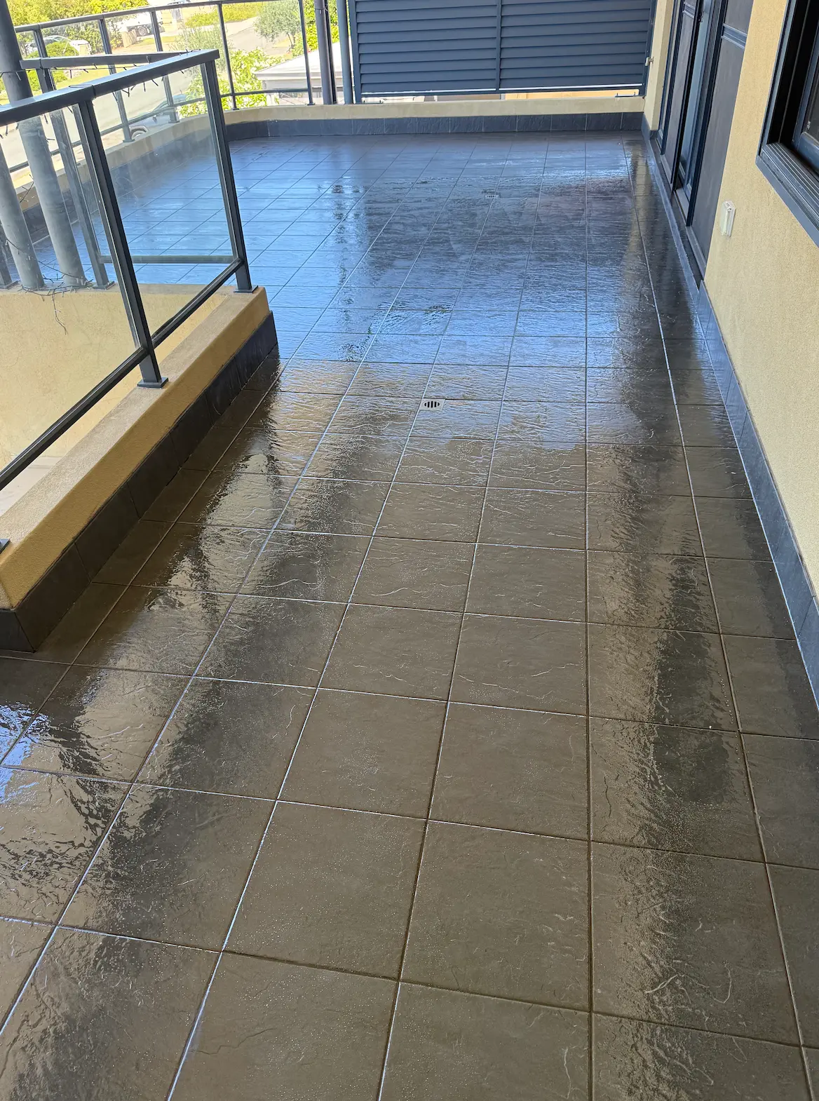 Balcony tiles freshly sealed with a clear wet-look sealer, showing a glossy dark finish and white grout lines