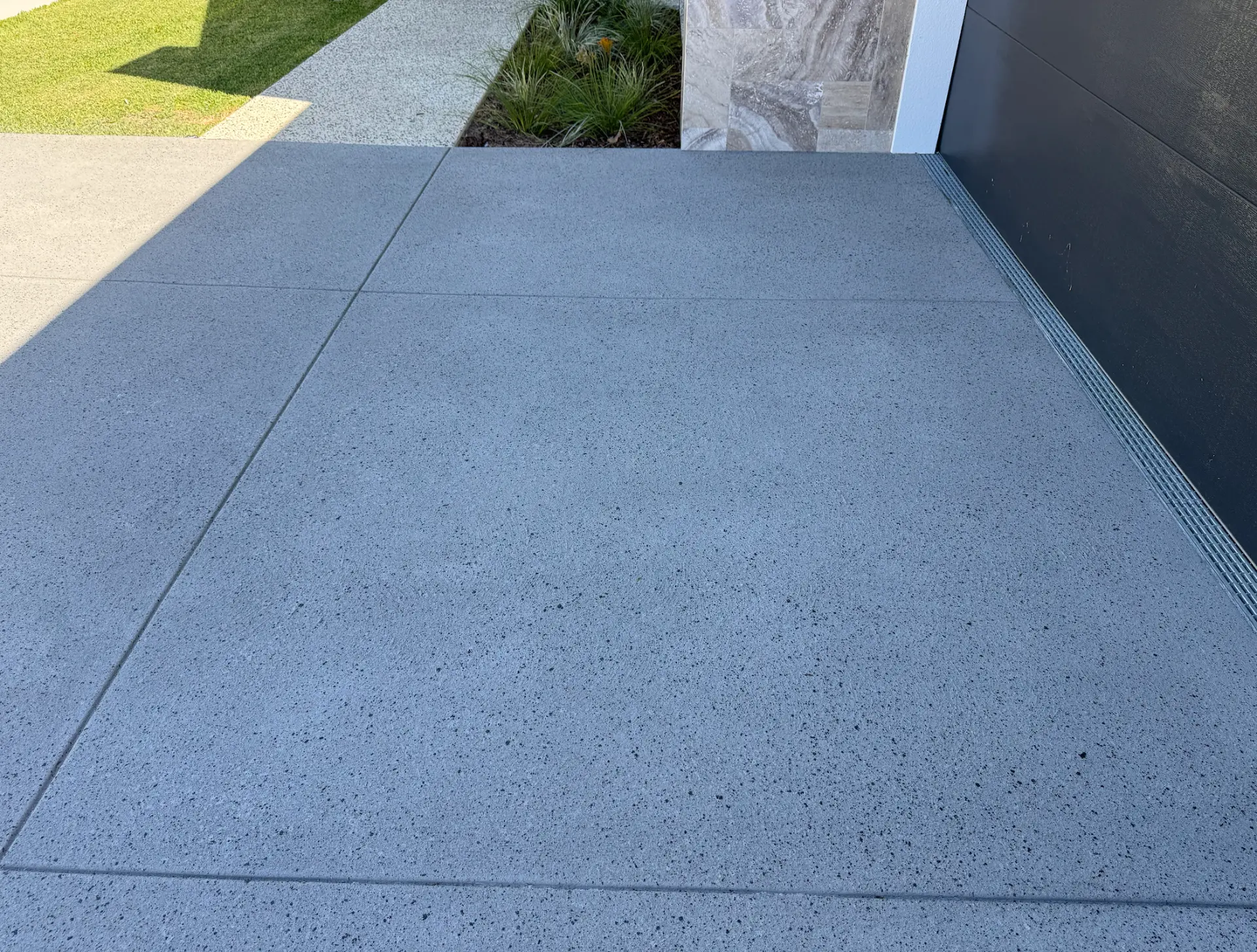 Silver-grey exposed aggregate style spray-on concrete entrance path with clean saw-cut joints beside a rendered home