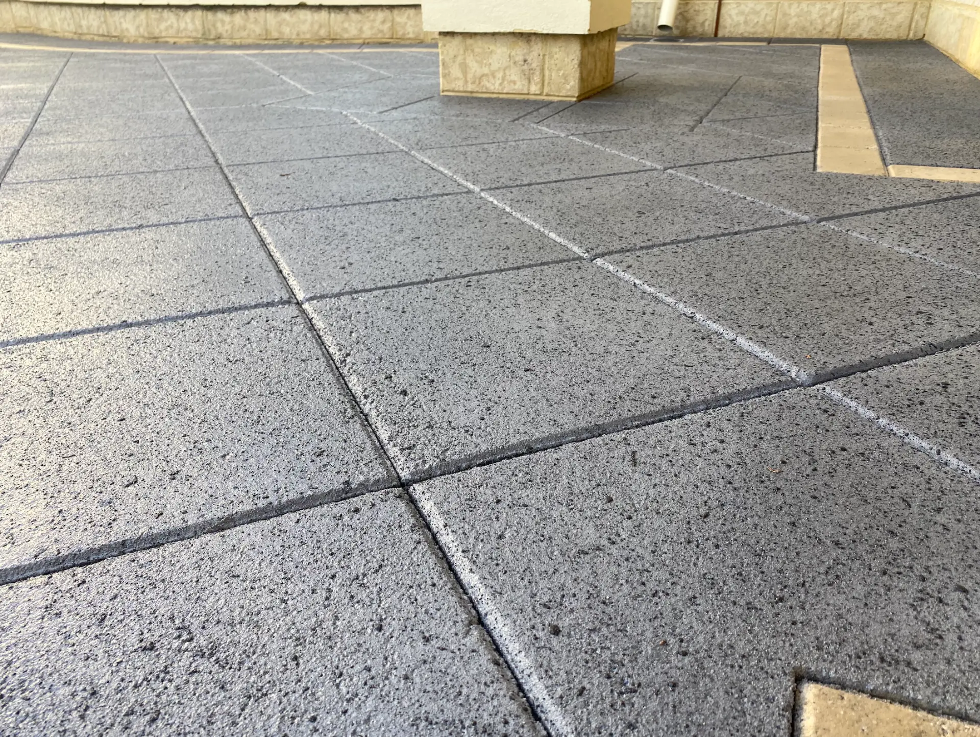Charcoal spray-on concrete scored into square tiles with pale border stones around a pillar base at a Perth home