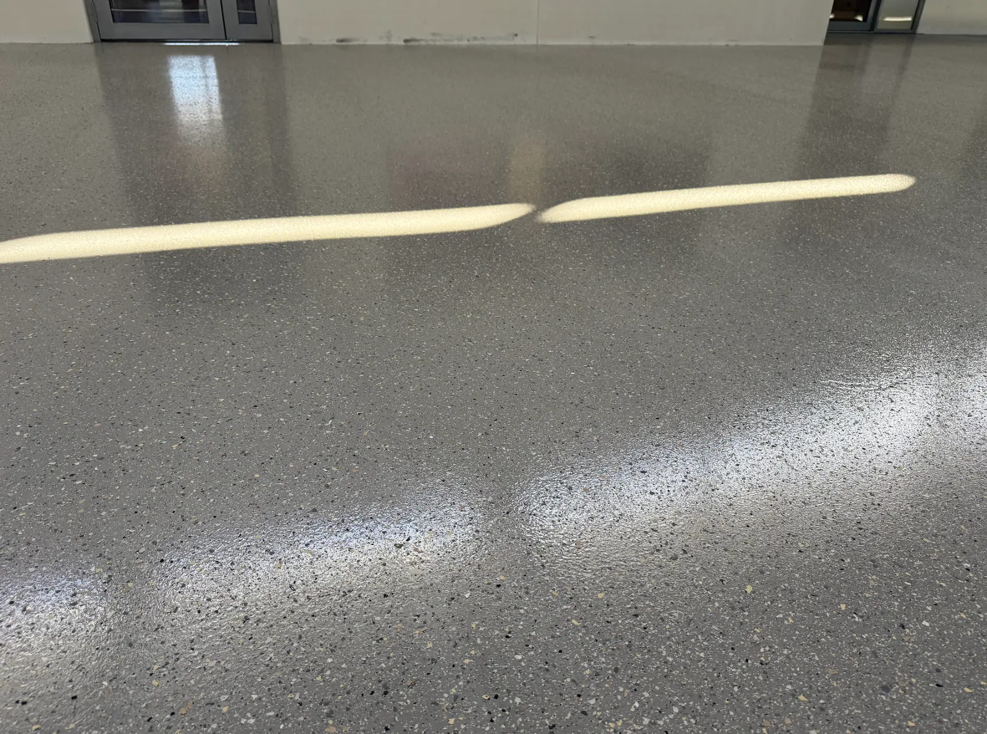 Grey speckled epoxy floor in a commercial building with sunlight streaming across the gloss finish