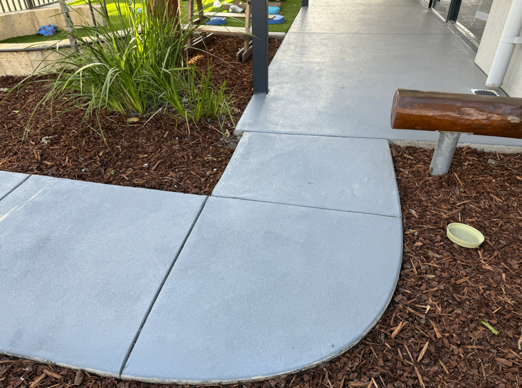 Freshly colour-sealed light grey concrete path curving through a landscaped garden bed with a smooth satin finish