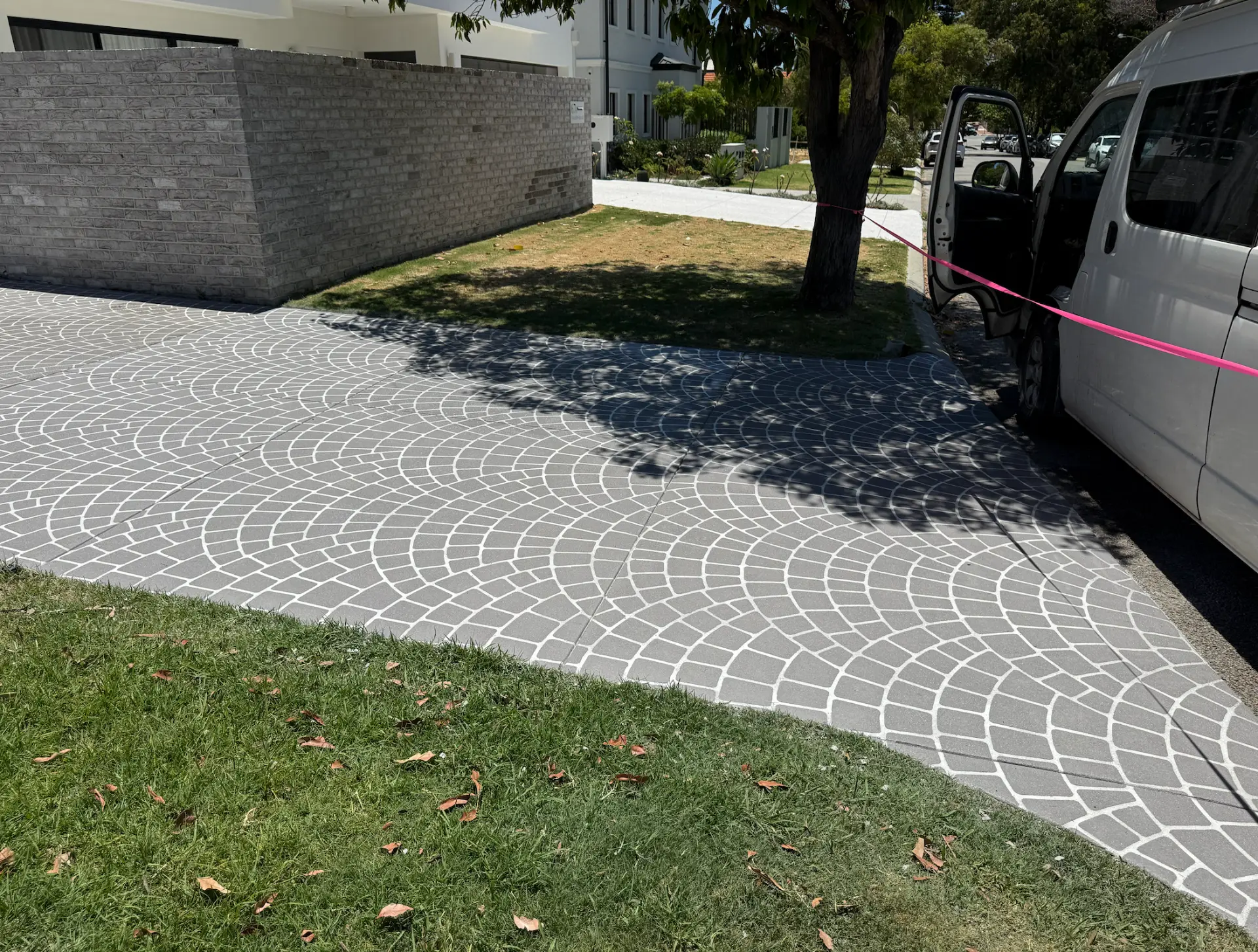 Grey fan cobble stencil spray-on concrete driveway with white joint lines beside a brick wall and grass verge