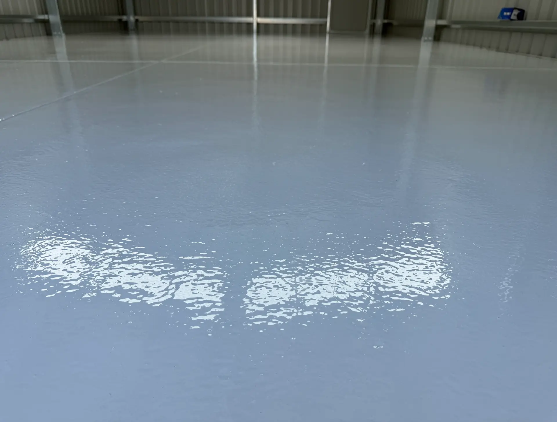 Glossy plain grey epoxy floor coating in an industrial shed, reflecting overhead light across the seamless finish