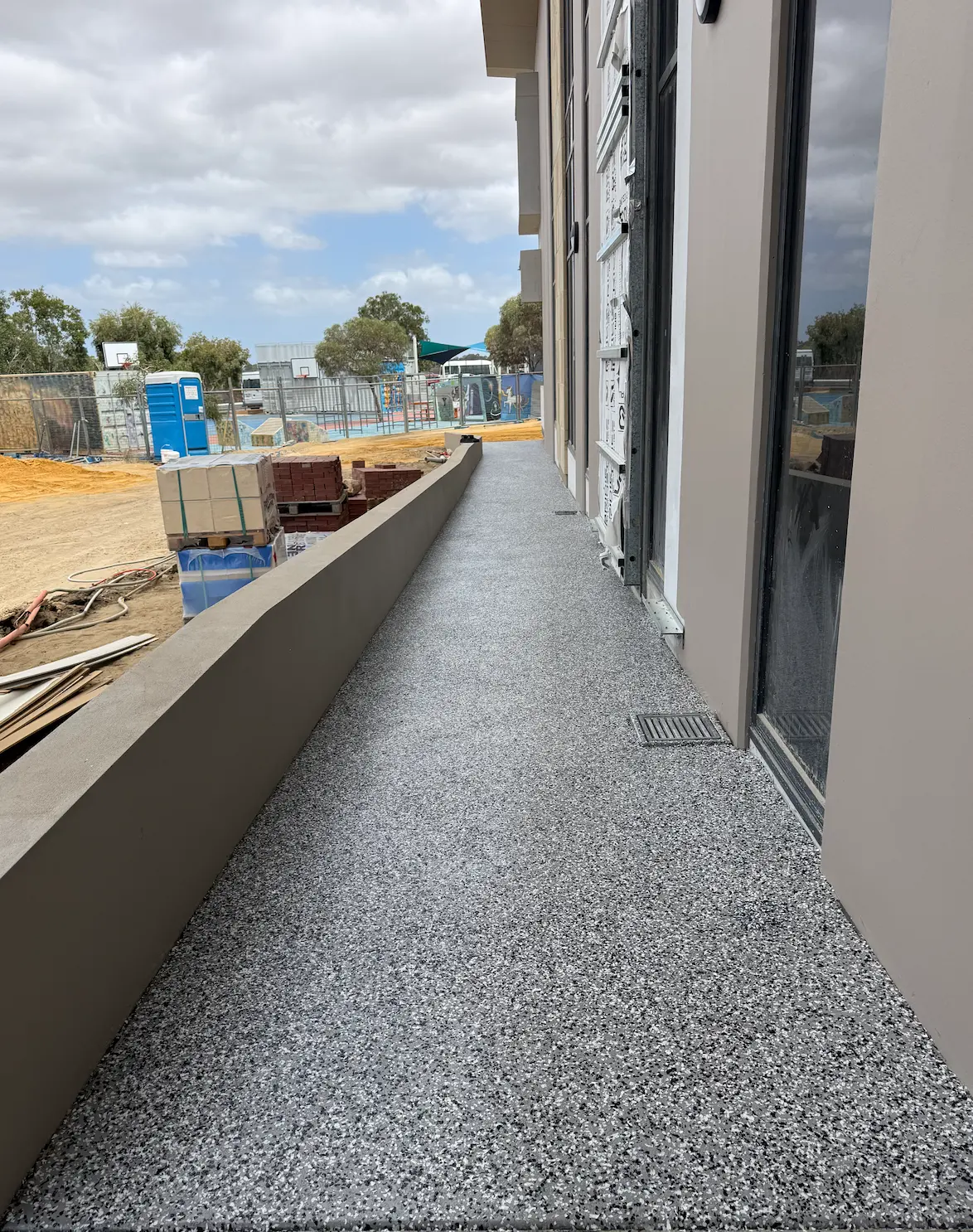 Grey and black epoxy flake coating along a new commercial building walkway with a drainage grate