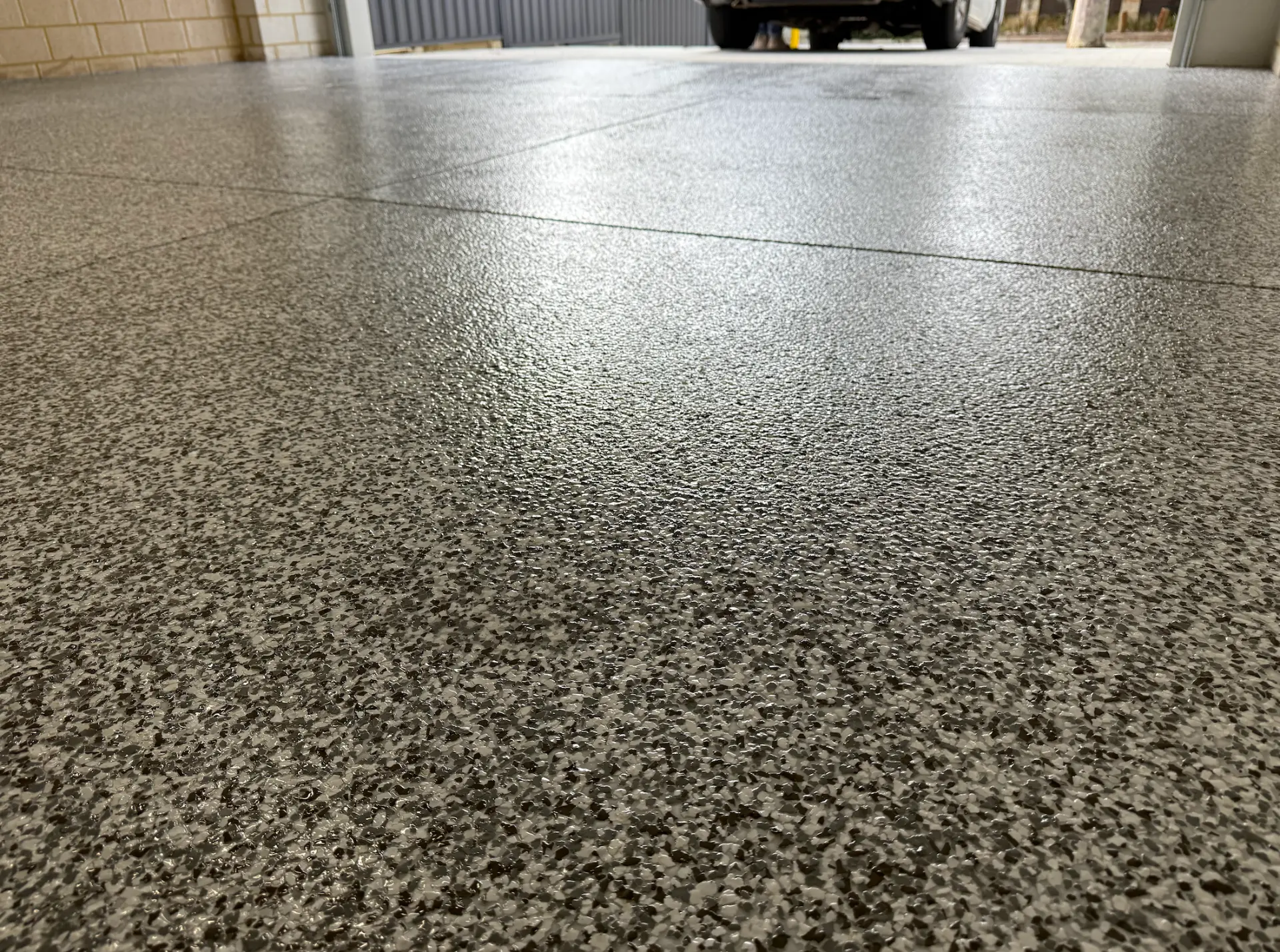 Glossy grey and white epoxy flake garage floor with a vehicle parked at the open door