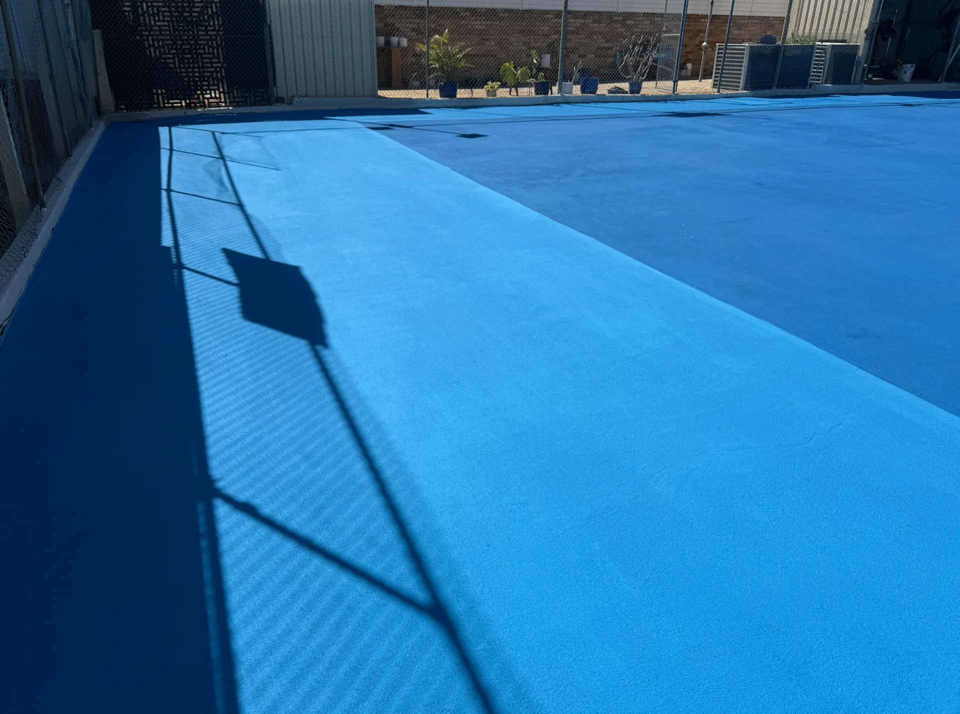 Close view of the light blue StreetBond court surface texture with fence shadows falling across it