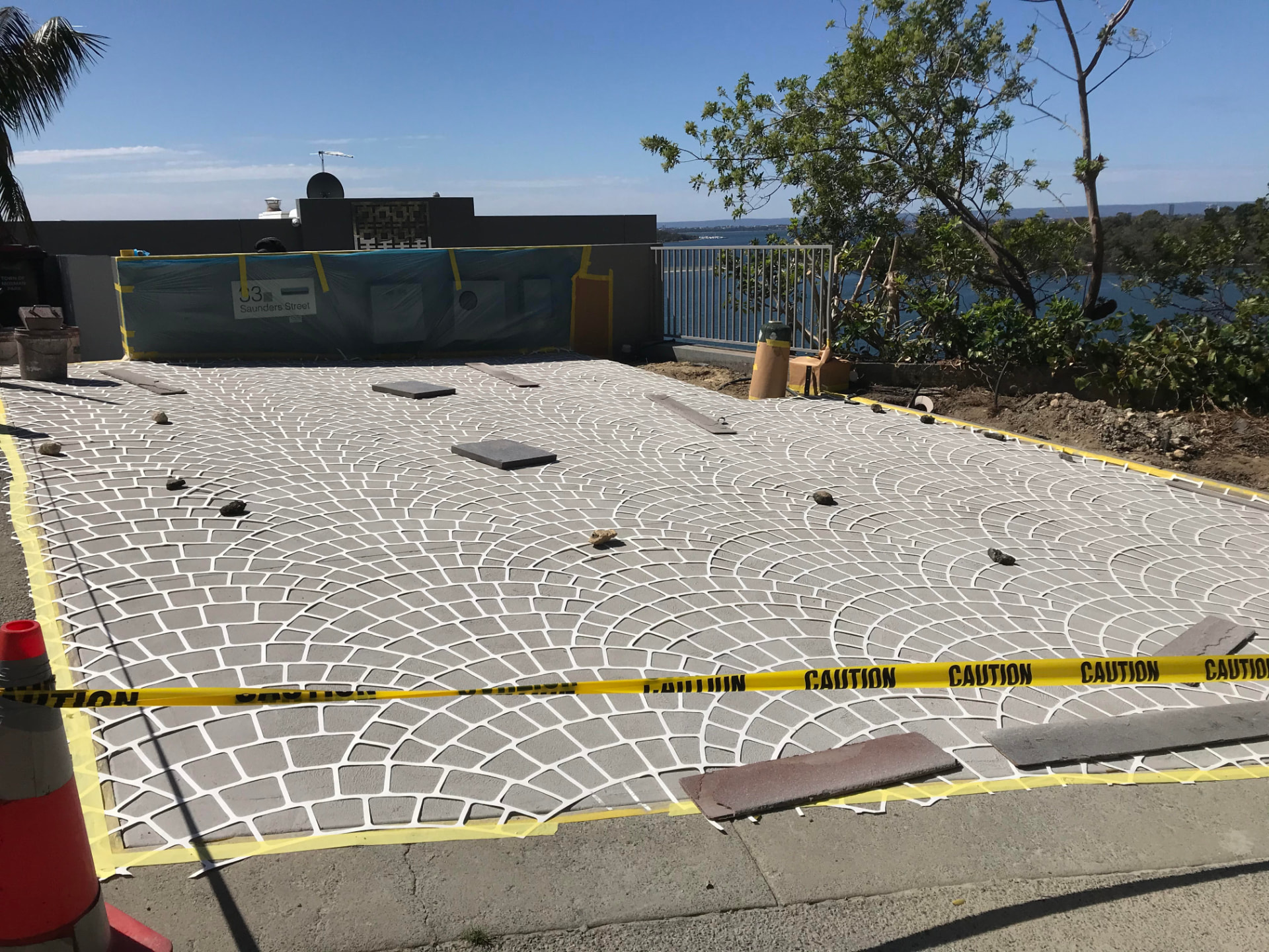 European fan cobble stencil taped down over the prepared driveway mid-application before the slate grey spray coat