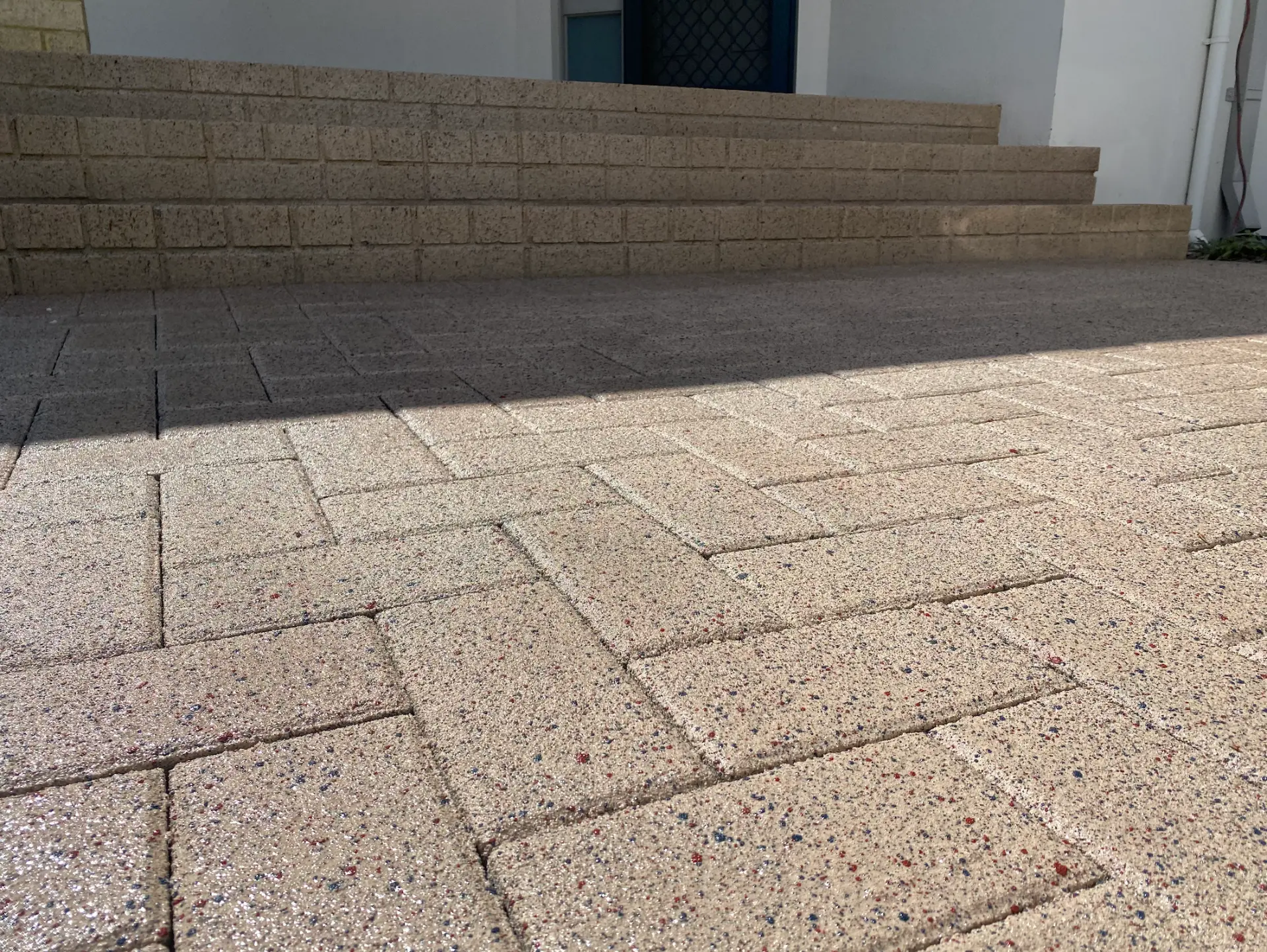 Herringbone brick pavers in sandy tones with rust and blue speckling, sealed, running up to entry steps