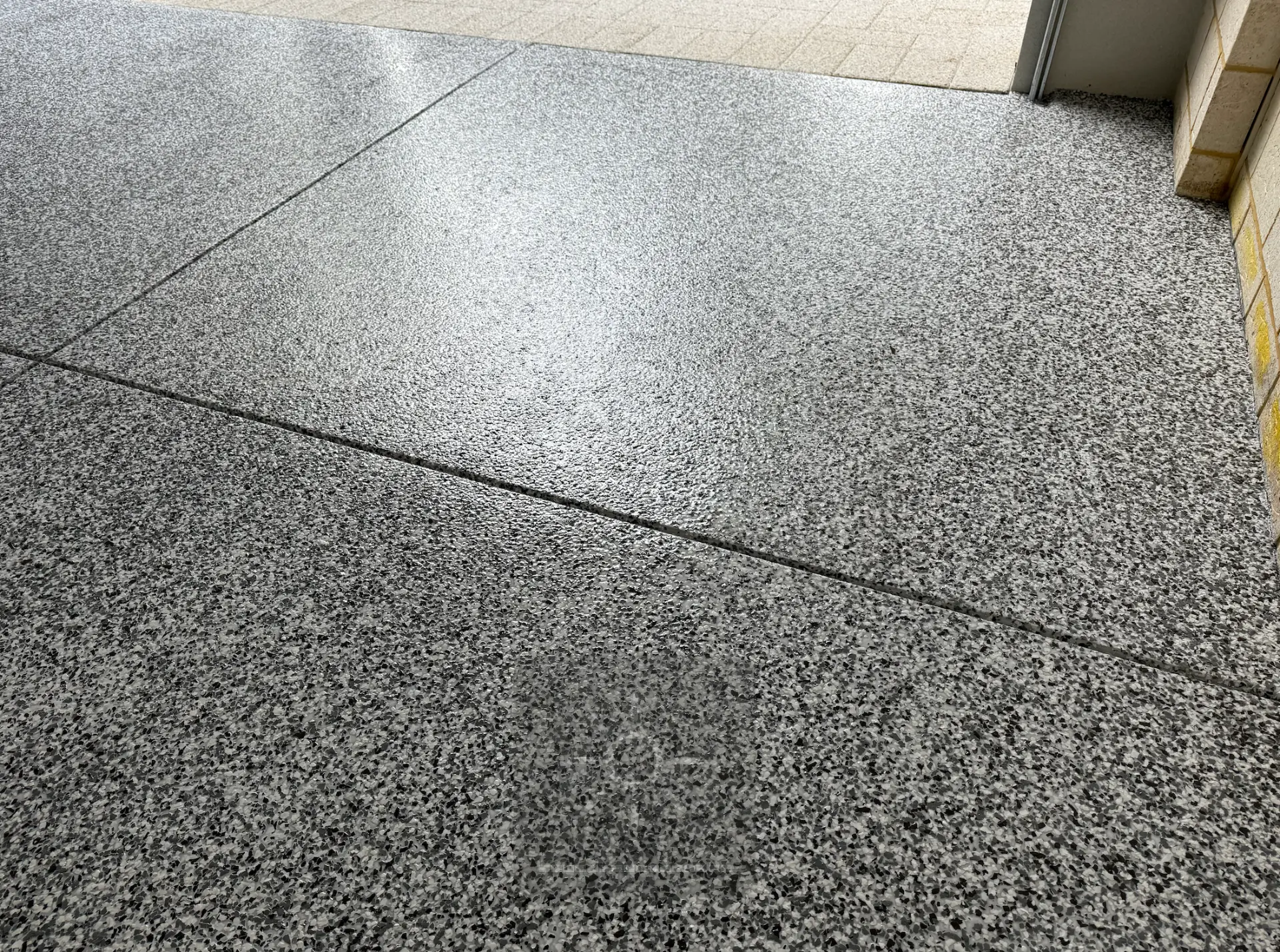 Black, grey and white epoxy flake floor coating running through an alfresco area beside limestone brickwork