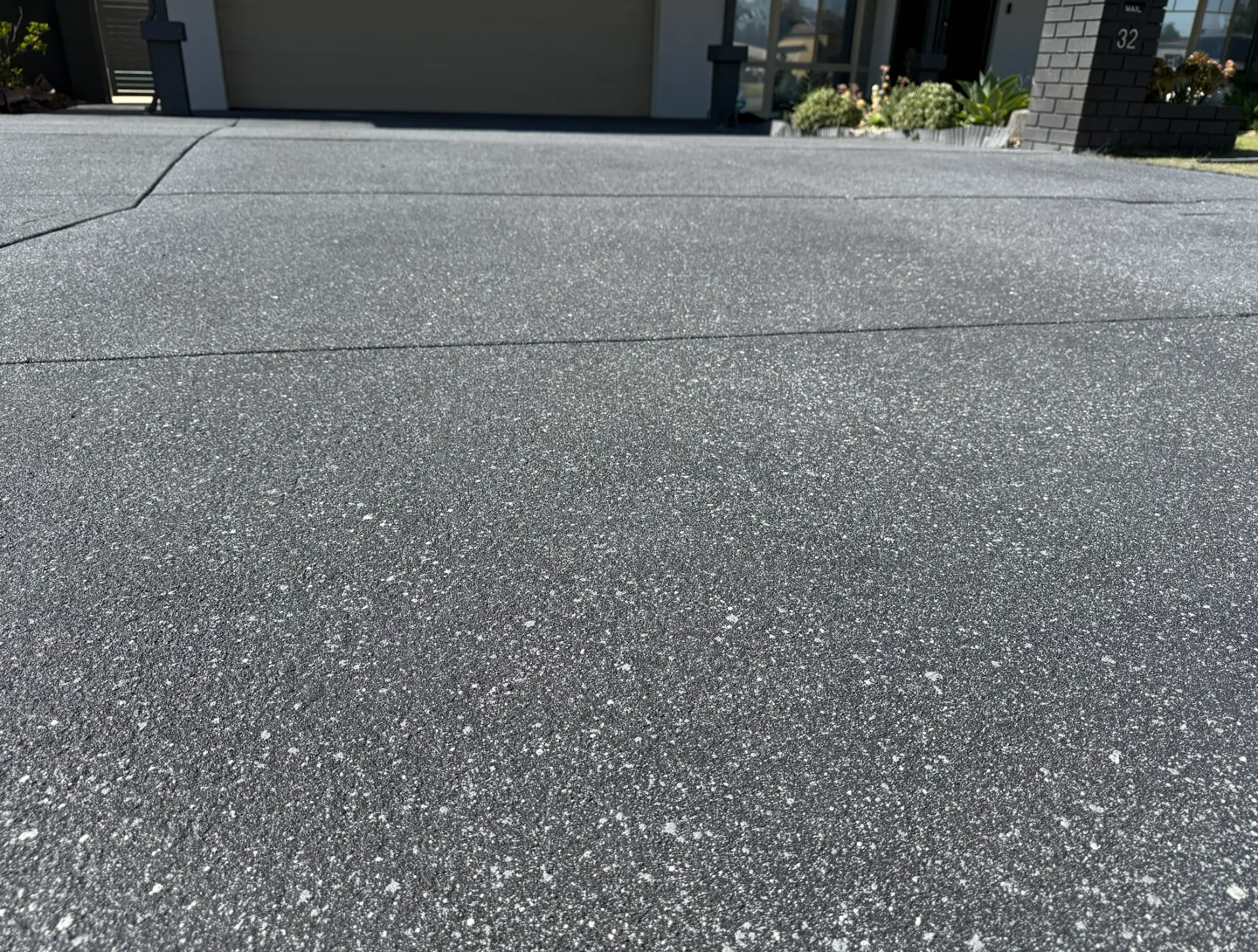 Charcoal exposed aggregate style spray-on concrete driveway with fine white and grey speckling across a modern Perth home