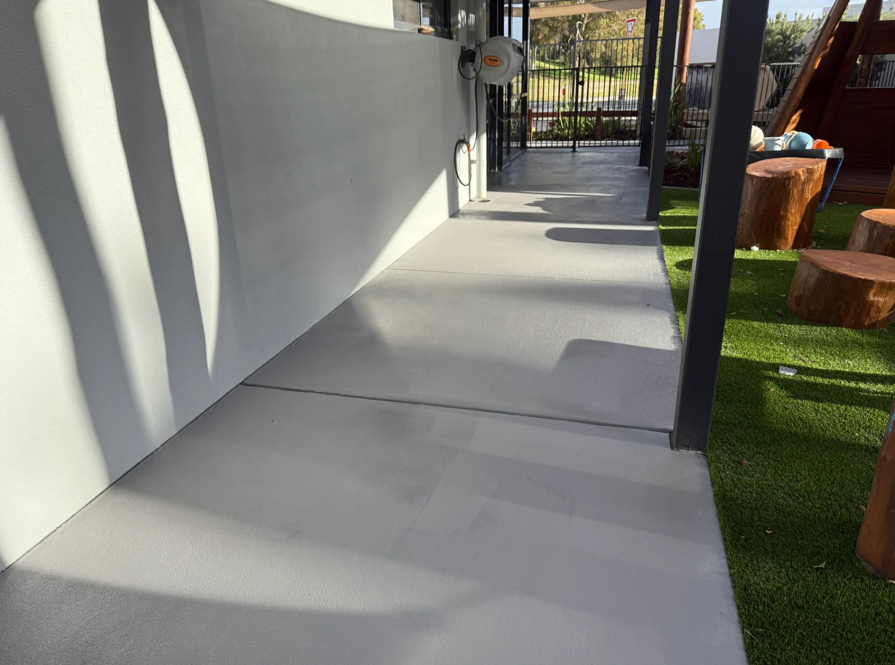 Plain concrete side path re-sealed in an even light grey with a clean satin finish beside artificial turf