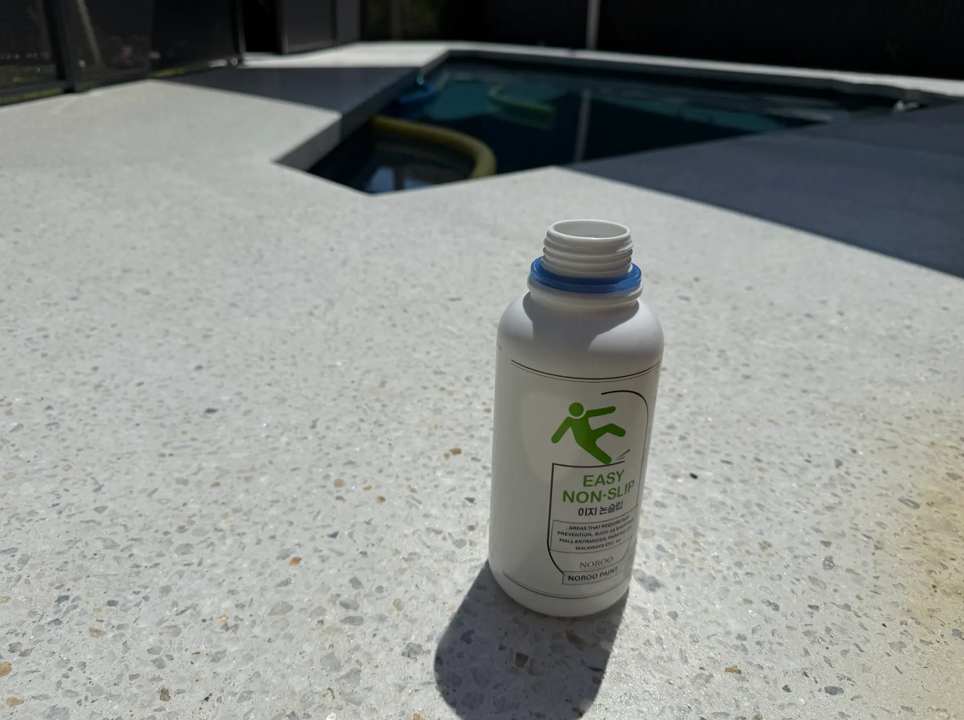 Easy Non-Slip clear sealer bottle on a light exposed aggregate pool surround, used to restore slip resistance to sealed concrete