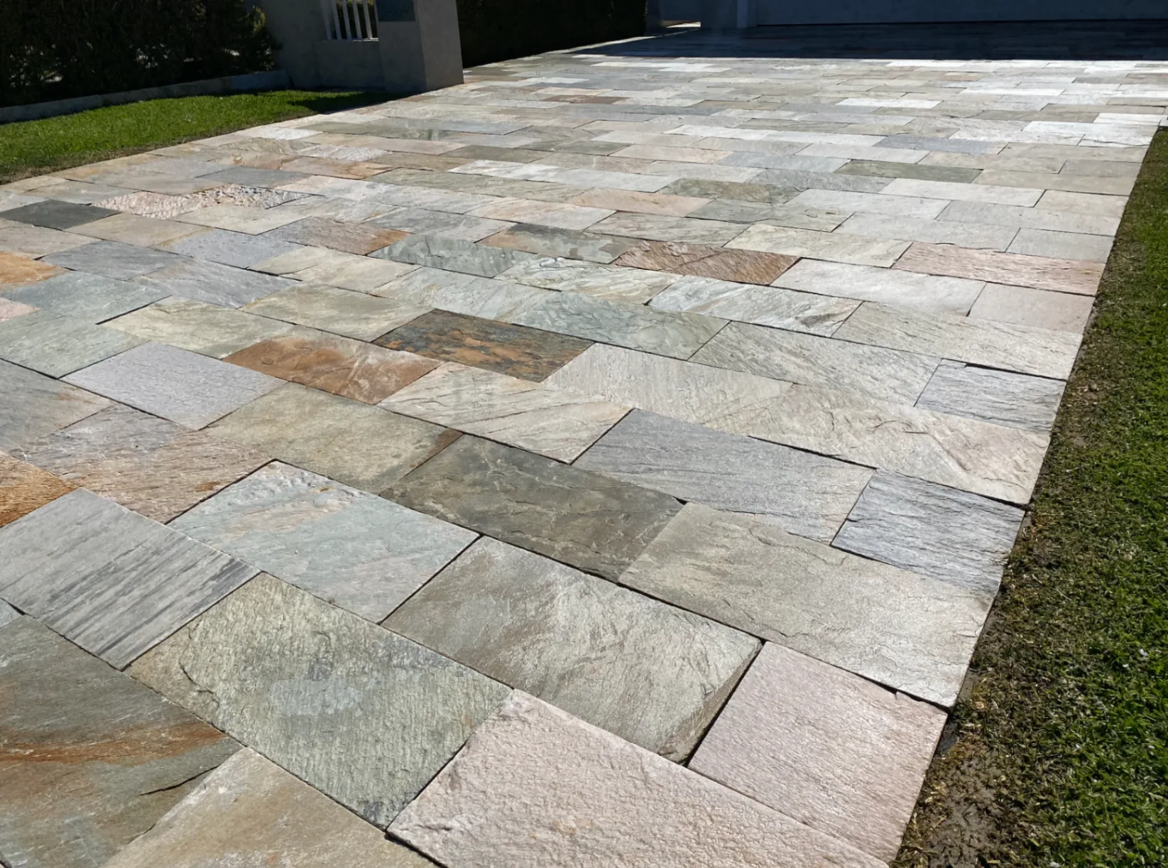 Sealed natural stone driveway in mixed grey, green and pink tones running past a lawn edge in full sun