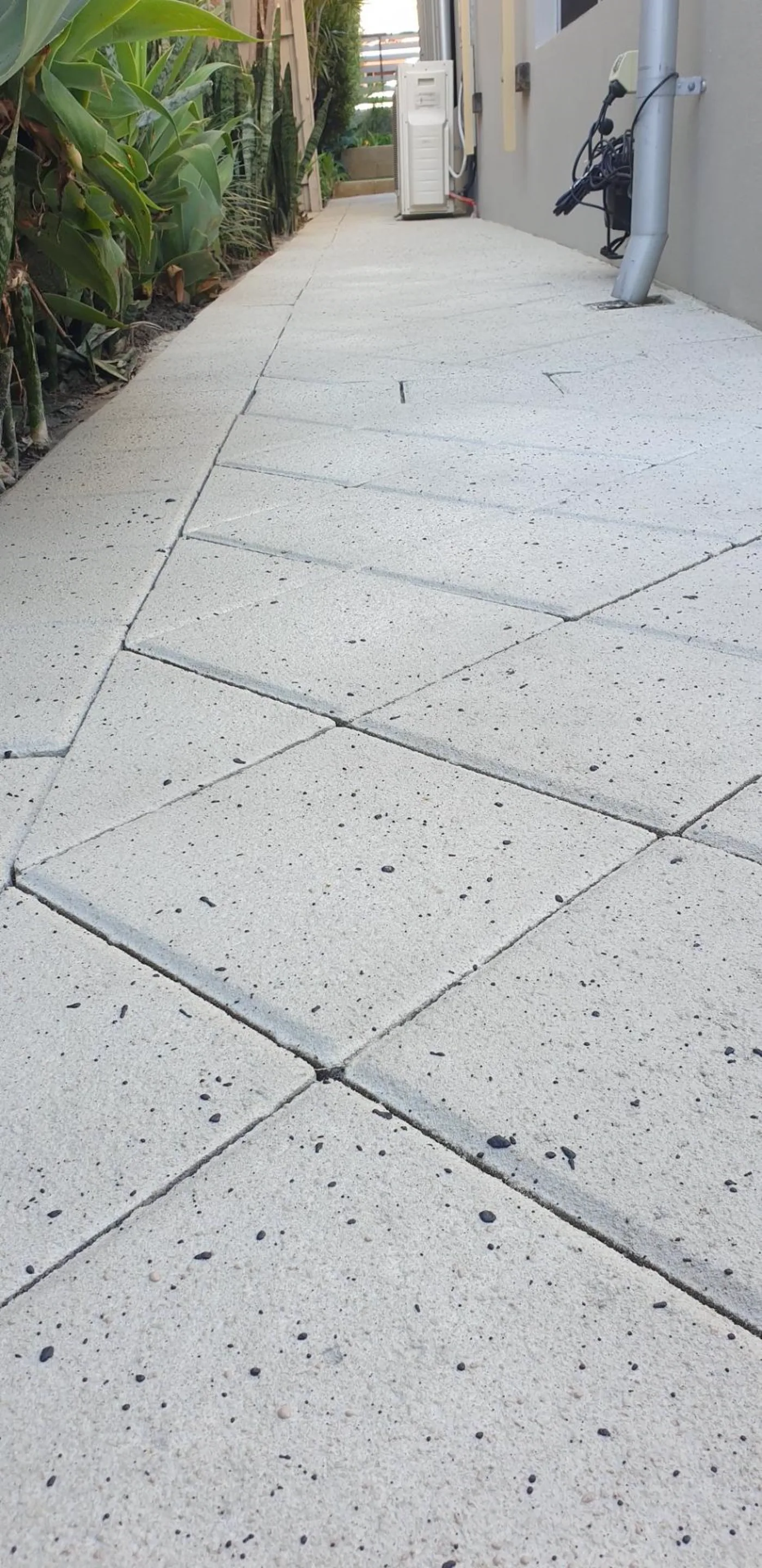 Off-white speckled exposed aggregate style spray finish in a large tile pattern along a side path