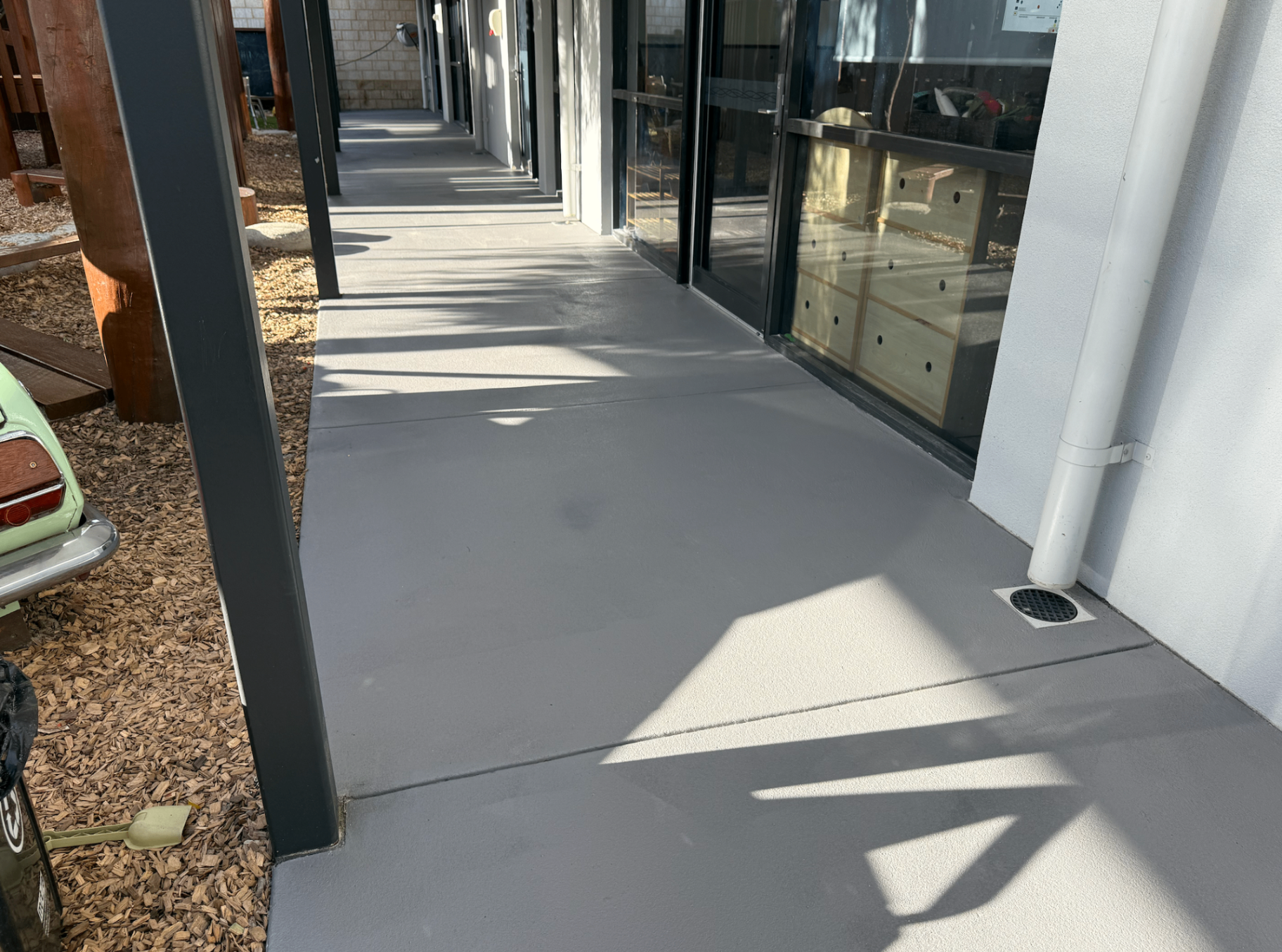 Re-sealed grey concrete veranda walkway beside a new home, evenly coated with a clean satin Colour & Clear Sealer finish