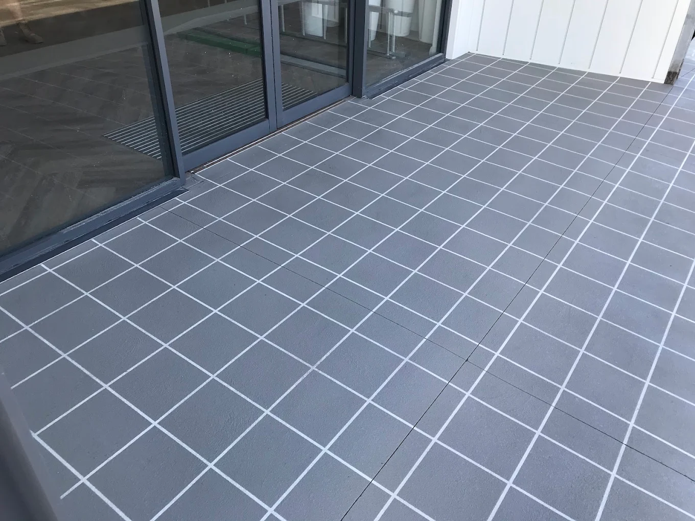 Grey stencil concrete in a square tile pattern with white joints across a covered balcony