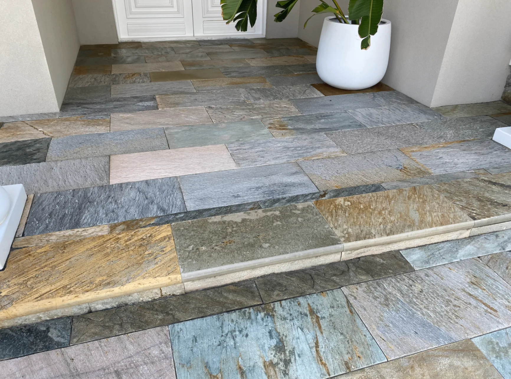 Freshly sealed natural stone entry paving with warm and grey tones brought back to full colour beside a bullnose step