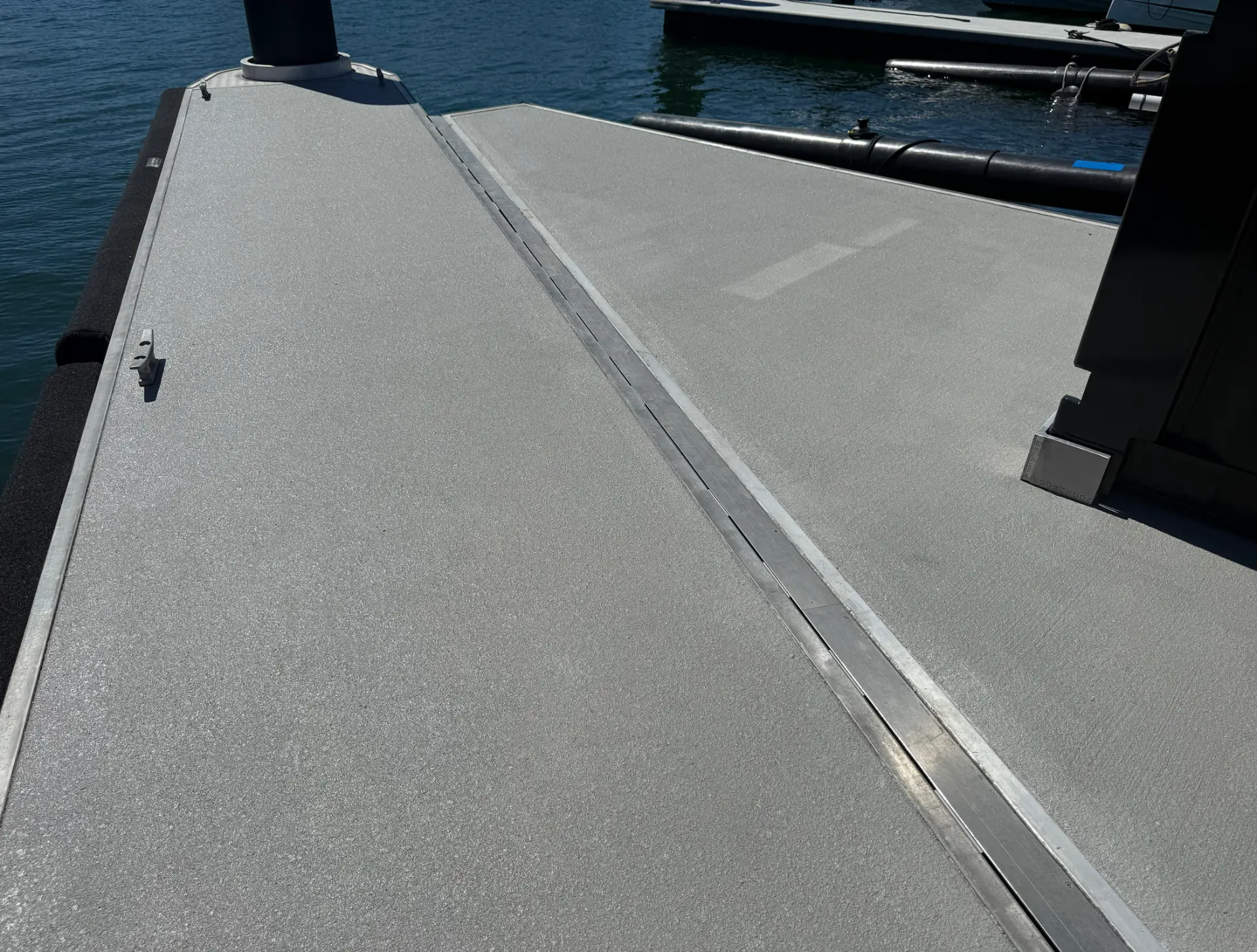 Plain grey spray-on concrete finish on a marina walkway deck, showing an even sealed finish with no pattern