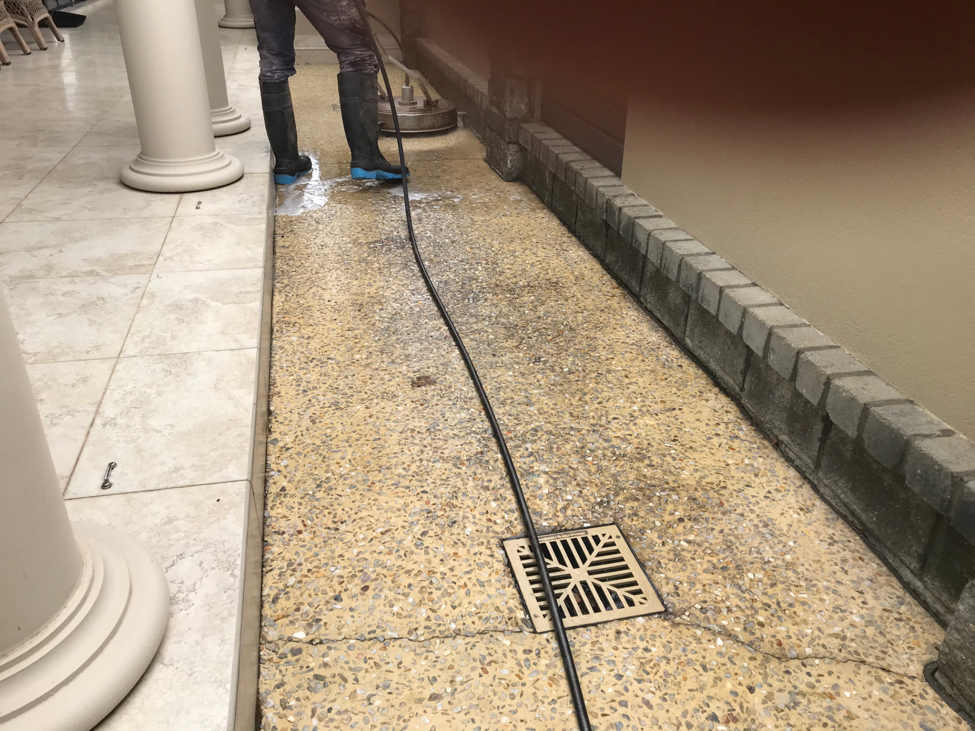 Dirty, stained exposed aggregate path before pressure cleaning and re-sealing beside a tiled alfresco area
